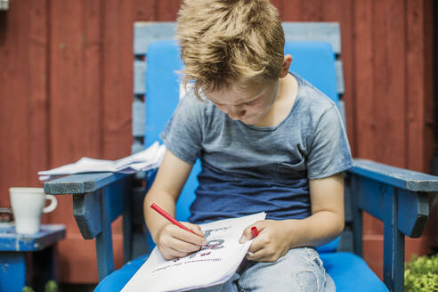 Junge zeichnet in blauem Stuhl im Freien - FOLF11633