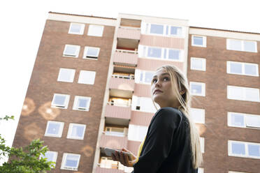 Young woman with smart phone by apartment building - FOLF11714