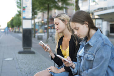 Schwestern mit Smartphone in der Stadt sitzend - FOLF11719