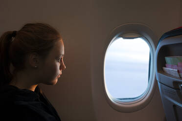 Teenage girl looking out airplane window - FOLF11722