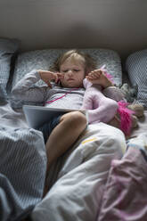 Girl lying in bed with wireless tablet and stuffed toy - FOLF11724
