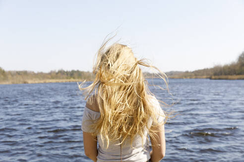 Rear view of windswept woman with blond hair by sea - FOLF11725