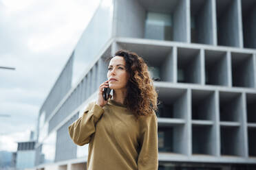 Geschäftsfrau, die vor einem Bürogebäude mit einem Mobiltelefon spricht - JOSEF10979