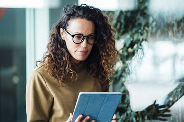 Businesswoman wearing eyeglasses using tablet PC in office - JOSEF10993