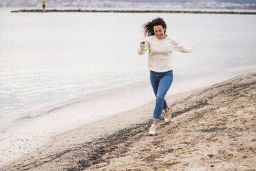 Cheerful woman running on sand at beach - JOSEF11008