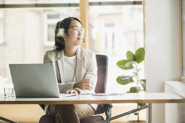 Contemplative businesswoman wearing headset at work place - UUF26727