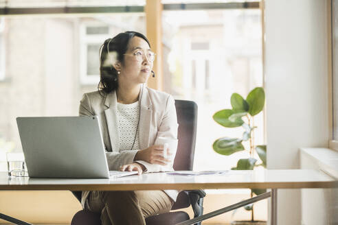 Nachdenkliche Geschäftsfrau mit Headset am Arbeitsplatz - UUF26727