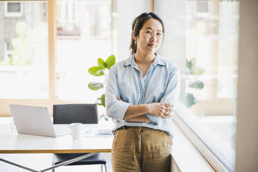 Smiling businesswoman with arms crossed by window - UUF26737