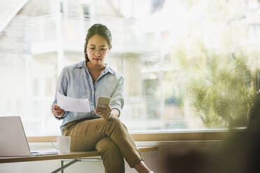 Businesswoman with document and smart phone at office - UUF26738