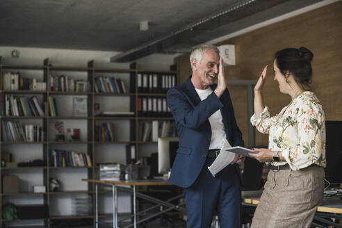 Happy business colleagues giving high-five standing by desk in office - UUF26757