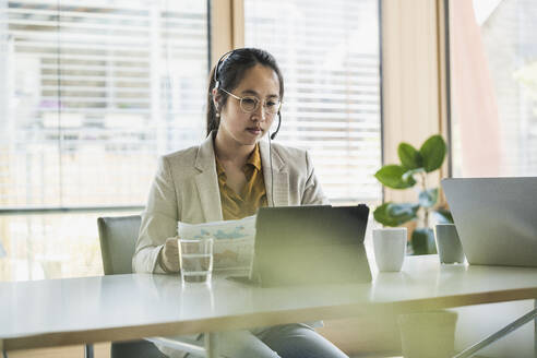 Geschäftsfrau mit Headset bei der Arbeit an einem Tablet-PC im Büro - UUF26761