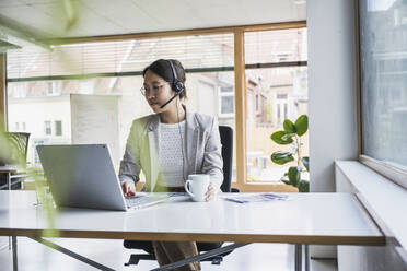 Smiling businesswoman working on laptop in office - UUF26766