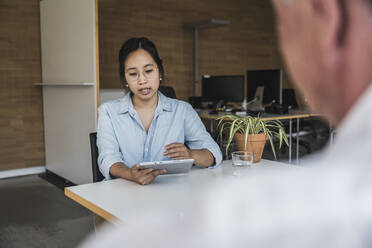 Businesswoman using tablet PC and discussing work with colleague at desk - UUF26780