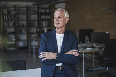 Contemplative businessman with arms crossed at work place - UUF26788