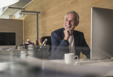 Happy senior businessman with desktop PC at work place - UUF26811