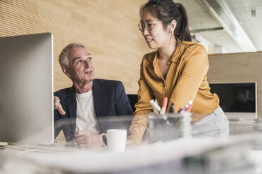 Lächelnder Geschäftsmann mit einem Kollegen, der am Computer im Büro diskutiert - UUF26812