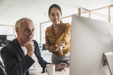 Glückliche Geschäftsfrau mit einem Kollegen, der über einen Desktop-PC im Büro diskutiert - UUF26813