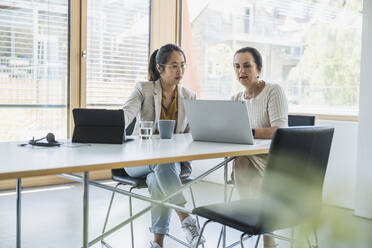 Mature businesswoman with colleague discussing over laptop in office - UUF26814