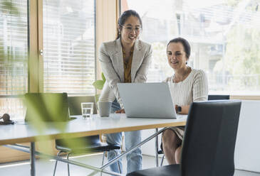 Happy businesswoman discussing work with colleague at work place - UUF26817