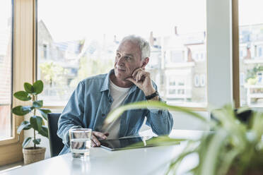 Thoughtful businessman with tablet PC sitting at desk - UUF26823