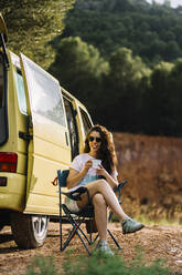 Frau mit Kaffeetasse an einem Lieferwagen sitzend, Aragonien, Spanien - DAMF01005