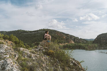 Frau sitzt auf einem Felsen unter bewölktem Himmel, Aragonien, Spanien - DAMF01011