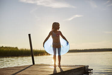 Mädchen im Badeanzug mit aufblasbarem Spielzeug am See bei Sonnenuntergang - FOLF11800