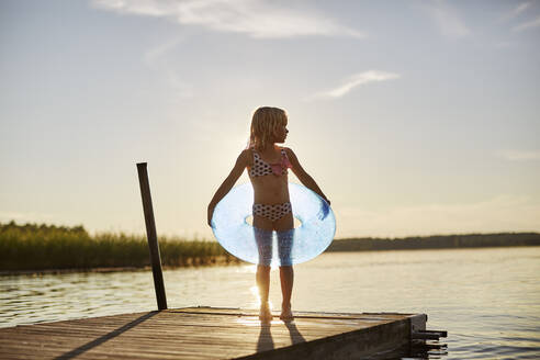 Girl in swimsuit with inflatable toy by lake at sunset - FOLF11800