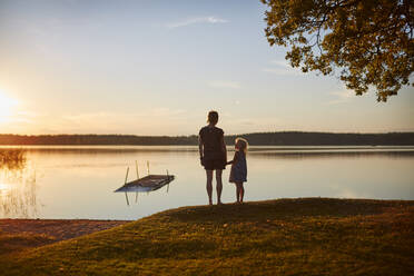 Frau und ihre Tochter stehen am See bei Sonnenuntergang - FOLF11801