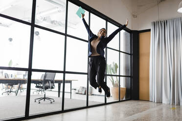 Happy young businesswoman jumping in office - DCRF01323