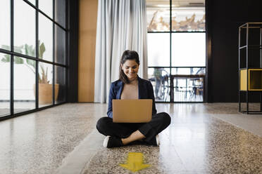 Smiling young businesswoman working on laptop at office - DCRF01325