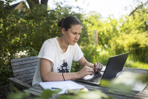 Teenager-Mädchen macht Hausaufgaben am Laptop am Tisch im Freien - FOLF11877