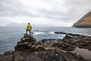 Faroe Islands, Eysturoy, Gjogv, Male hiker admiring Atlantic Ocean from edge of cliff - WPEF06094