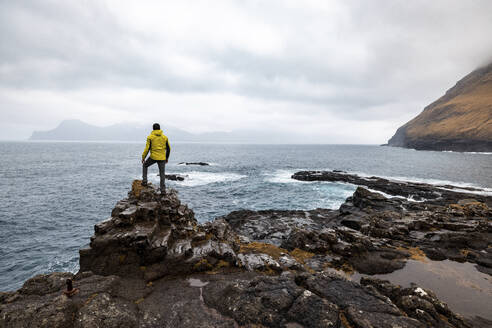 Faroe Islands, Eysturoy, Gjogv, Male hiker admiring Atlantic Ocean from edge of cliff - WPEF06094