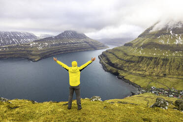 Färöer Inseln, Eysturoy, Funningur, Wanderer steht mit erhobenen Armen am Rand des Aussichtspunkts Hvithamar - WPEF06096