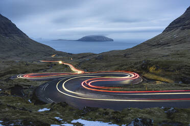 Faroe Islands, Streymoy, Vehicle light trails stretching along remote winding road - WPEF06100