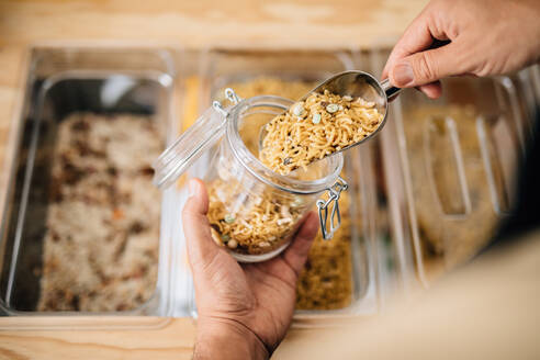 Back view of anonymous female pouring dry pasta inside glass jar in local store - ADSF35612