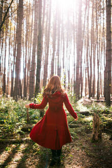 Back view of unrecognizable redhead female with outerwear standing in woods in fall - ADSF35618