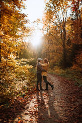 Full body side view of happy young couple standing embracing looking at each other in autumn forest in national park in canada - ADSF35624