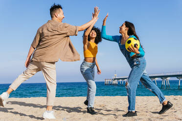 Full Body diverse Mann und Frauen mit Ball lächelnd und geben hohe fünf zu einander, während die Zeit auf Sandstrand in der Nähe von Meer auf Sommerwochenende Tag am Strand - ADSF35637