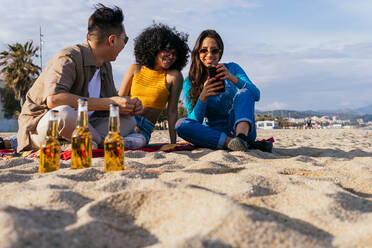 Von unten glücklich multiethnischen Mann und Frauen lächelnd und Surfen in den sozialen Medien auf Handys beim Ausruhen am Strand auf sonnigen Sommertag auf Resort - ADSF35639