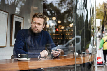 Älterer Geschäftsmann mit Smartphone in einem Café sitzend - JOSEF11033