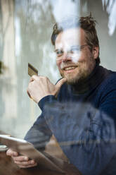 Lächelnder Geschäftsmann mit Tablet-PC und Kreditkarte in einem Café sitzend - JOSEF11036