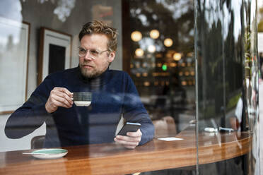 Geschäftsmann mit Smartphone und Kaffeetasse in einem Café sitzend - JOSEF11038
