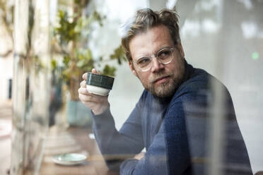 Geschäftsmann mit Brille hält Kaffeetasse in einem Café - JOSEF11043