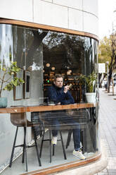 Mature businessman sitting in coffee shop seen through glass window - JOSEF11046