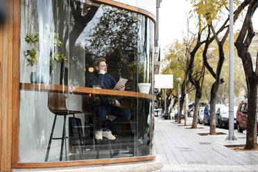 Geschäftsmann mit Tablet-PC in einem Café sitzend, gesehen durch ein Glasfenster - JOSEF11047