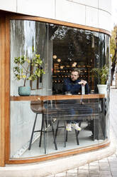 Businessman in cafe seen through glass window - JOSEF11049