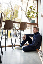Contemplative businessman sitting on floor in coffee shop - JOSEF11051