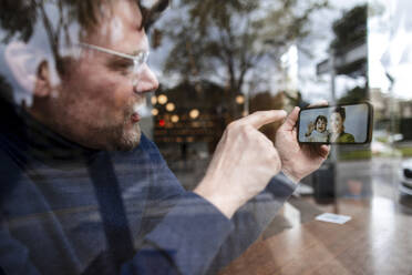 Geschäftsmann zeigt auf Tochter bei Videoanruf über Smartphone in Café - JOSEF11054